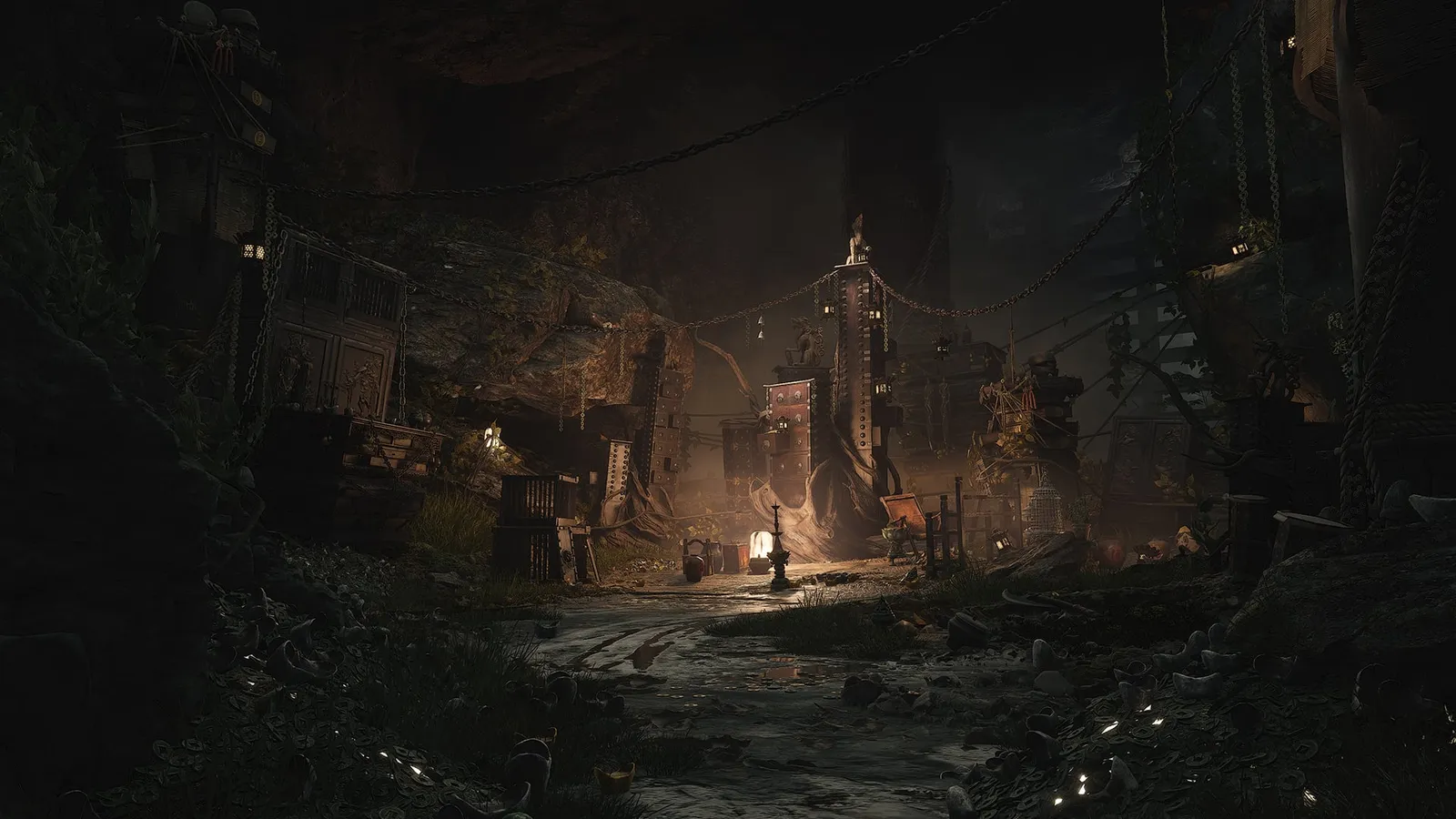 Dark cavern settlement with warm lantern light, hanging chains and wooden scaffolding stacked around a central tower.