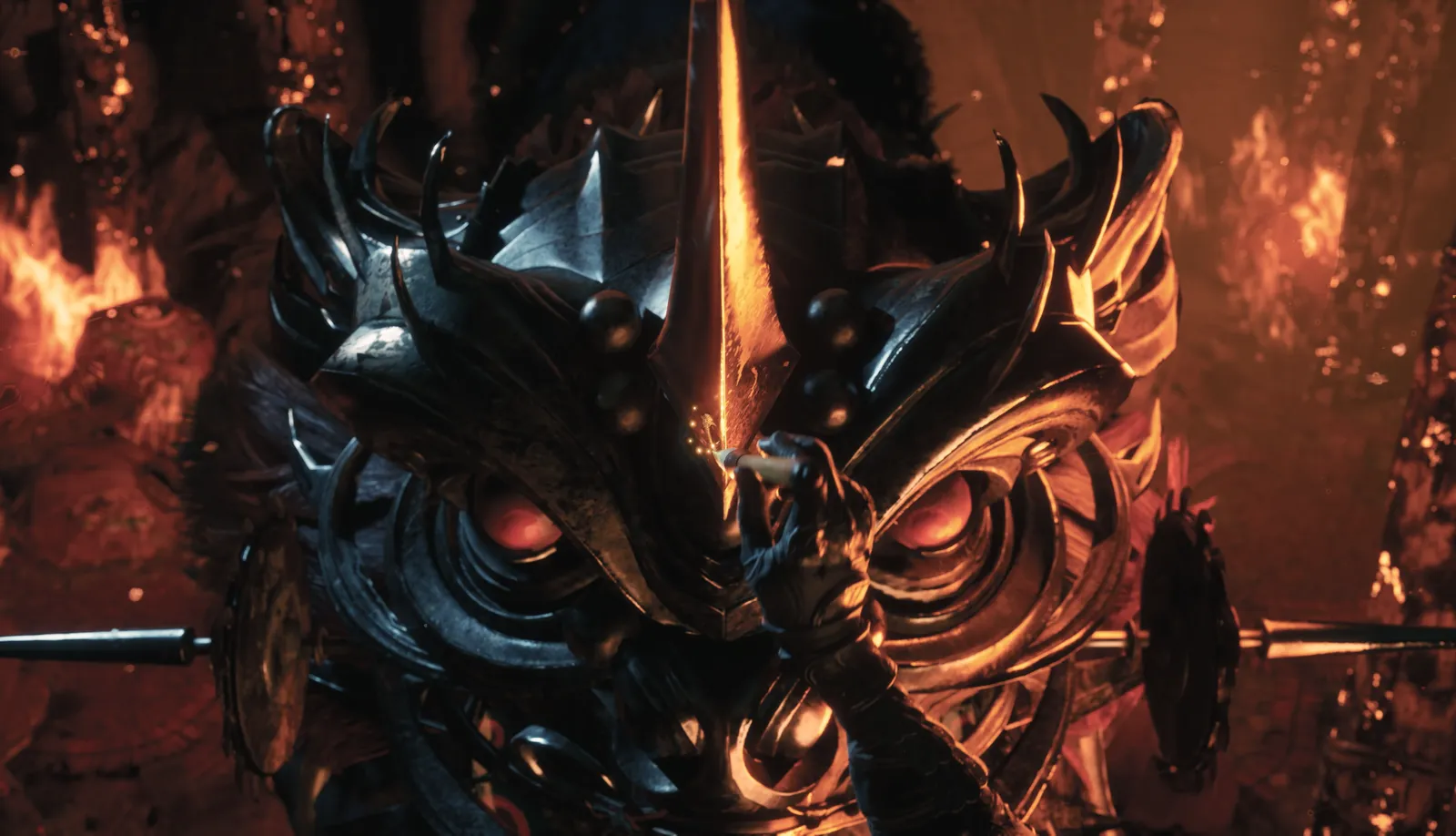 Extreme close-up of an ornate spiked black metal mask with glowing red eyes amid flames, a thin spear tip pointing up.